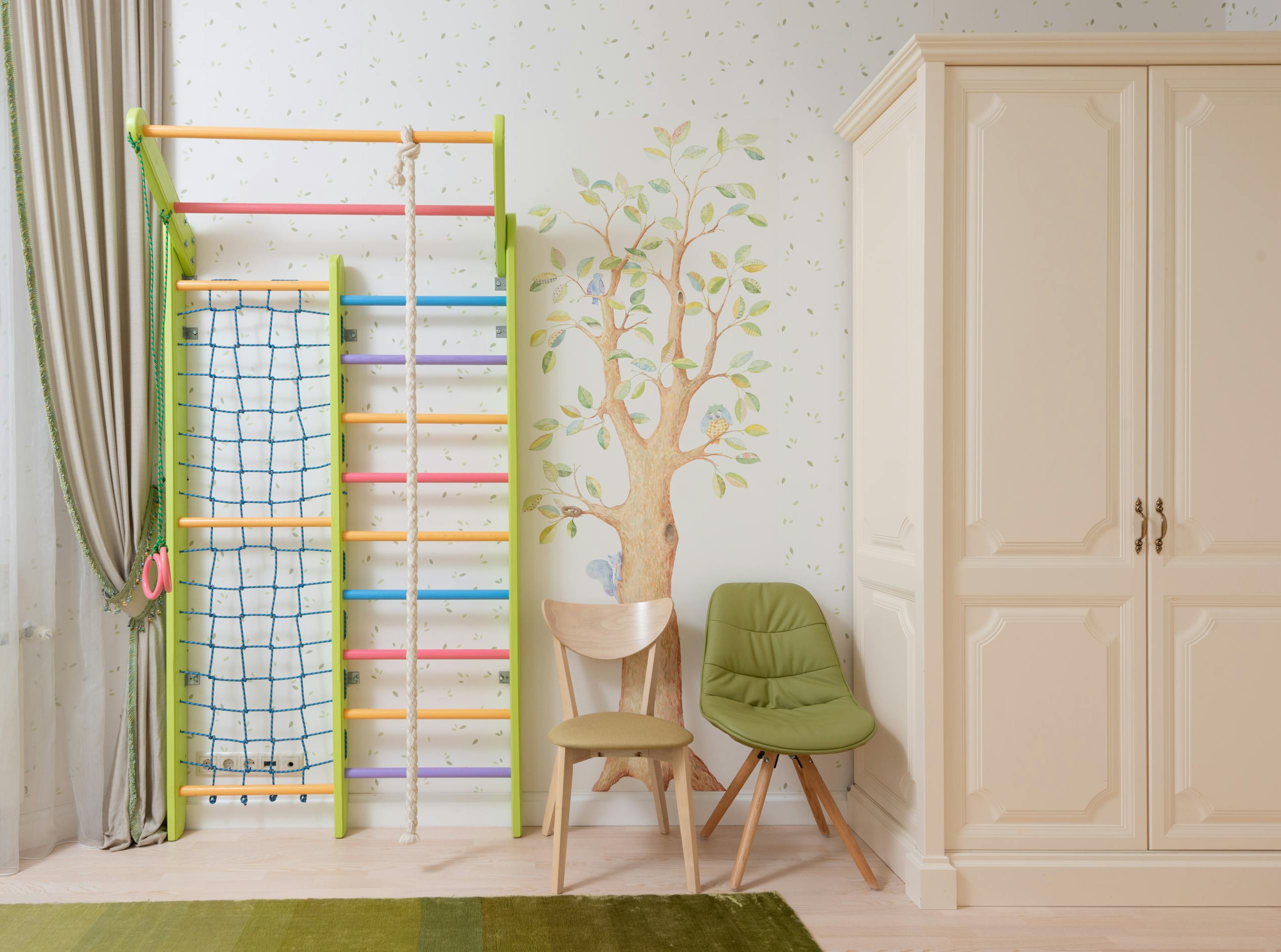 White wall with tree image in light bedroom for kid with wardrobe and colourful play area